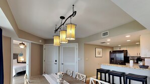 A modern kitchen with a central island, white cabinetry, and a stainless steel refrigerator. - Regency Towers #203 West | Beach + Pool Access! (Pensacola Beach)