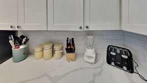 A kitchen counter with white cabinets, a blender, a toaster, and jars.