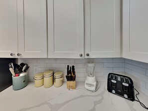 En køkkenbordplade med hvide skabe, en blender, en brødrister og krukker.