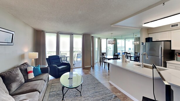 A modern living room with a sofa, a glass coffee table, and a dining area with chairs and a table.