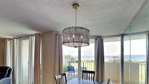 A dining area with a table and chairs, a hanging light fixture, and a view of the ocean through large windows.