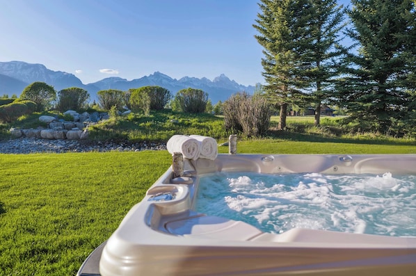 A hot tub with a mountain view, surrounded by grass and trees.