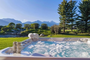Un bain à remous avec deux canettes de bière et des serviettes, entouré d’un paysage luxuriant avec des montagnes en arrière-plan.
