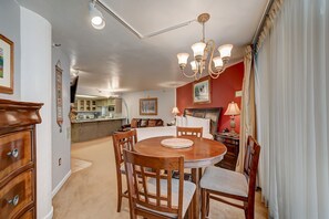 Un coin repas avec une table et des chaises en bois, un lustre et une cuisine en arrière-plan.