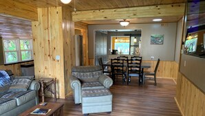L’intérieur chaleureux d’un chalet avec des murs en bois, un coin repas et un espace détente comprenant un canapé et un pouf.