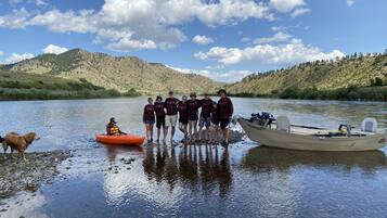 A group of people standing by a river with boats and a dog.