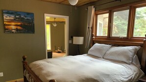 Une chambre à coucher avec un lit en bois, un tableau accroché au mur et une fenêtre avec des rideaux.