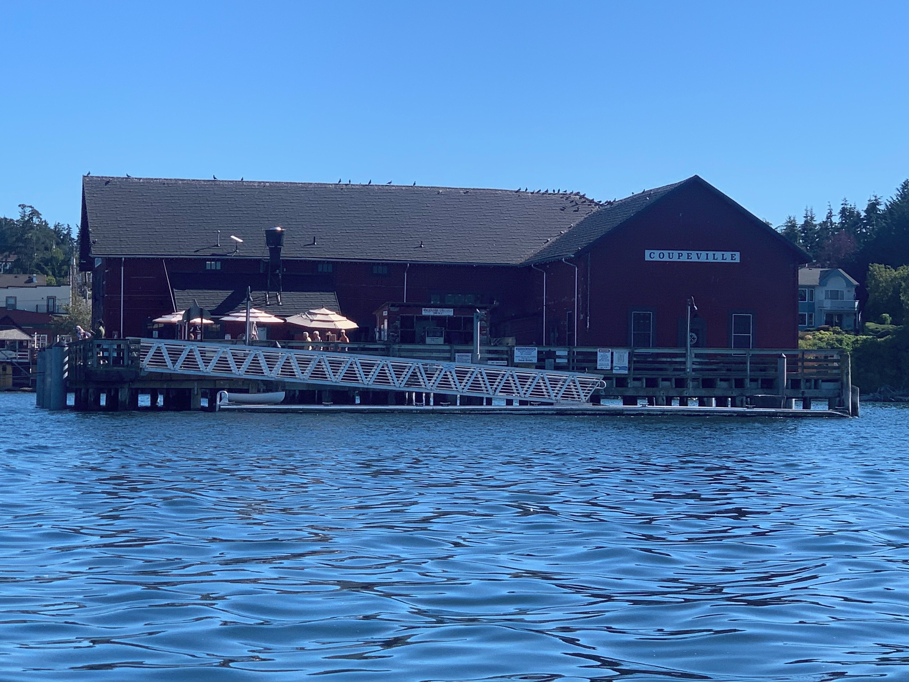 A red building with a sign reading "COUPEVILLE" on a dock extending into a body of water.