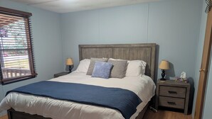 A bedroom with a wooden bed, two bedside tables with lamps, a window with blinds, and a wooden floor. - Cozy Cabin in the Mountains (Newland)