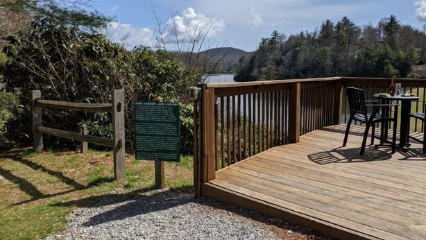 A wooden deck with a view of a lake and forest. - Cozy Cabin in the Mountains (Newland)