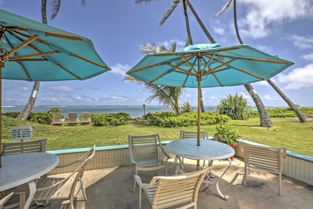 An outdoor seating area with tables and chairs, two umbrellas, and a view of the ocean.