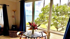 Une pièce avec vue sur la mer, une table à manger avec des chaises, un ordinateur portable, une lampe et un panier en osier.