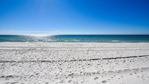 En strand med hvidt sand og krystalklart, blåt vand i stærk sol.