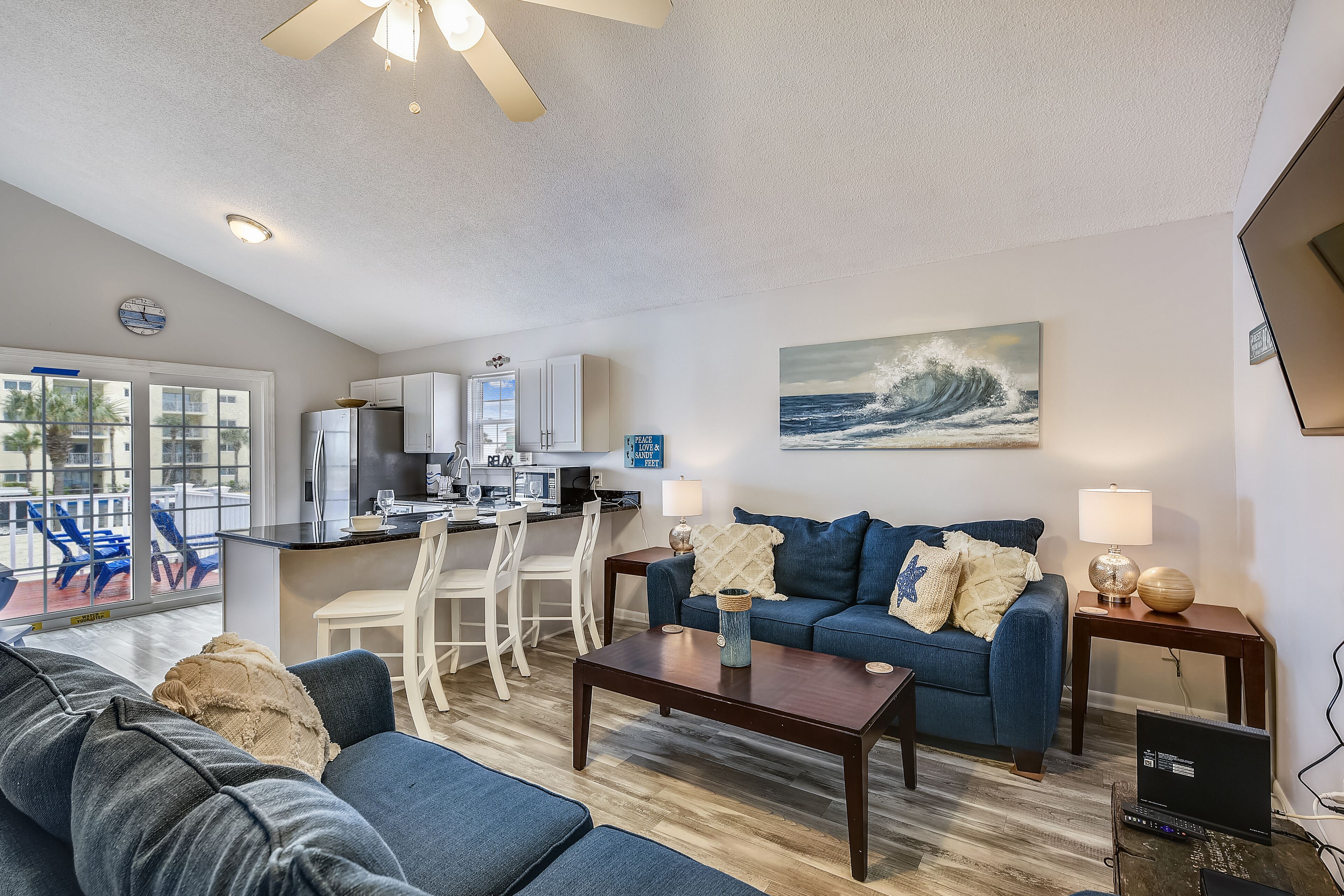 A modern living room with a blue sofa, a coffee table, and a dining area with a kitchen in the background.