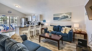 En moderne stue med en blå sofa, et sofabord og et spiseområde med et køkken i baggrunden.