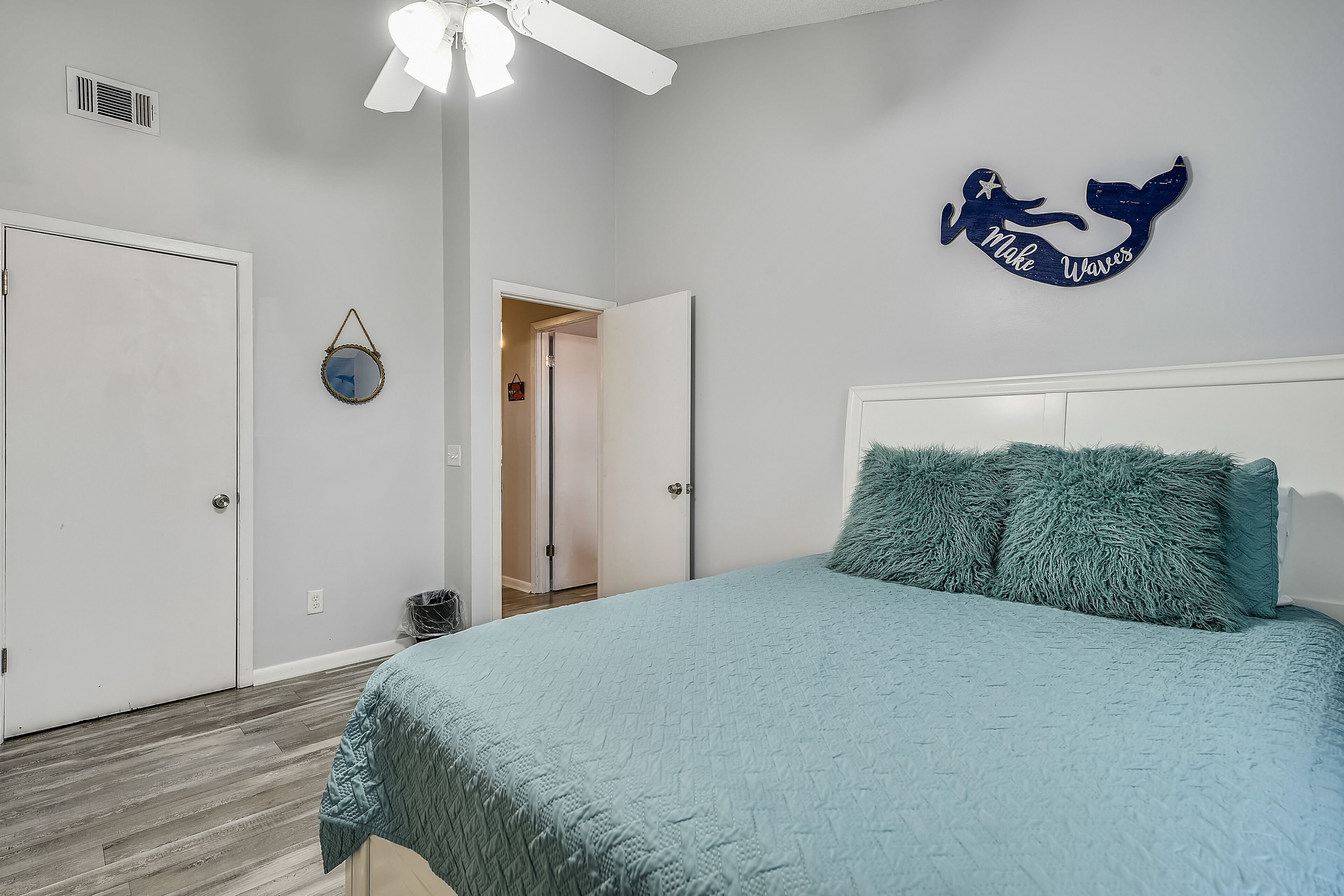 A bedroom with a bed, a ceiling fan, a wall decoration, and a door.