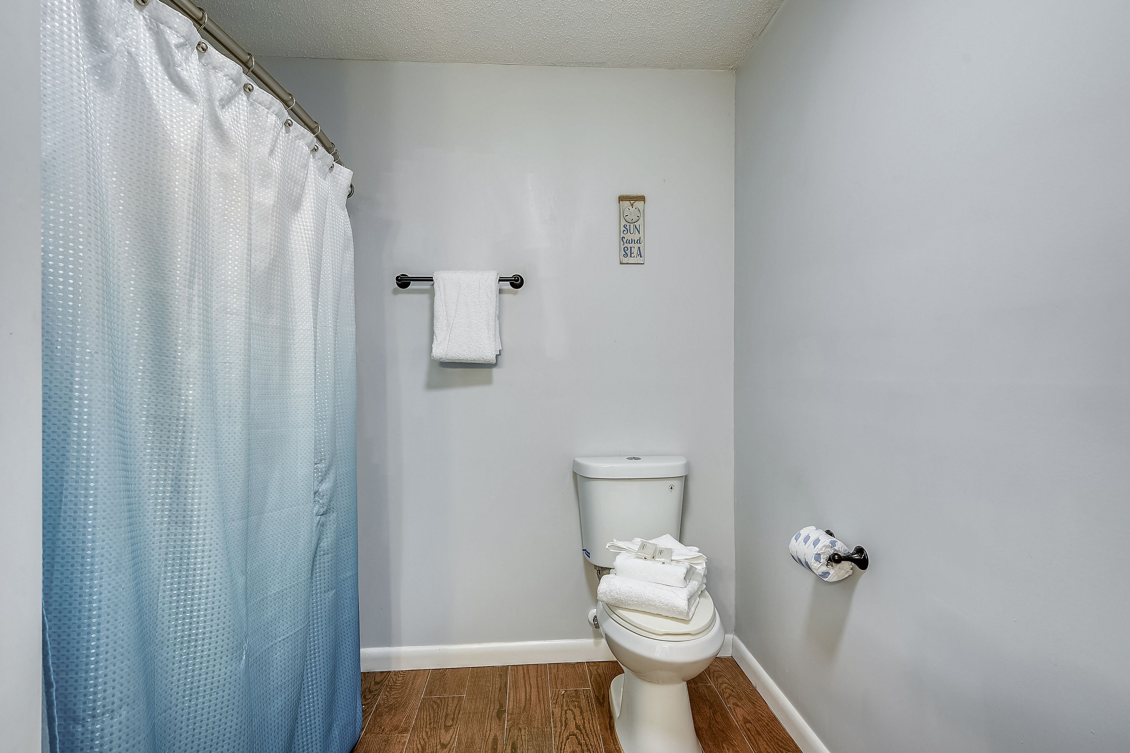 A bathroom with a shower curtain, a toilet with a towel on it, and a wall-mounted towel rack.