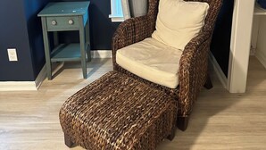 Ein Zimmer mit dunkelblauer Wand, ein Korbstuhl mit Kissen, ein kleiner Holztisch und ein Hocker aus Korbgeflecht.