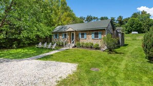 A two-story log cabin with a gravel driveway and a small porch. - Tara Cove Cottage (Ogunquit)
