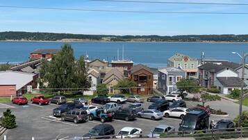 A parking lot with various vehicles, a waterfront view, and buildings in the background.