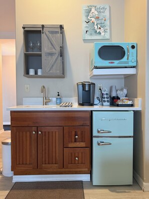 A compact kitchen with a wooden cabinet, a vintage Frigidaire refrigerator, a microwave, and a coffee maker.