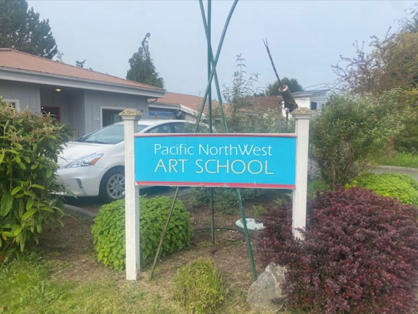Schild des Pacific NorthWest Art School, umgeben von Grünpflanzen und einem geparkten Auto.