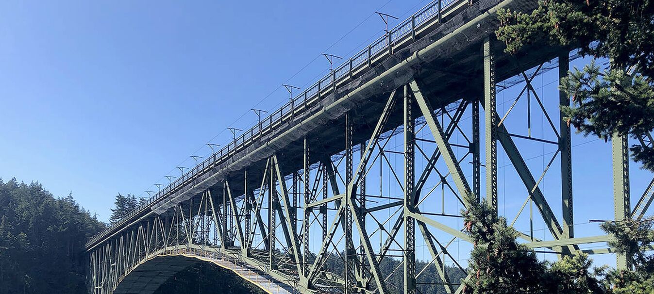 Un puente de acero con pasarela peatonal y un solo arco.