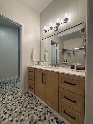 A bathroom with a tiled floor, wooden cabinets, a sink with a mirror, and a hairdryer mounted on the wall.