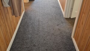 A hallway with a carpeted floor, wooden walls, and a door leading outside. - Womans Beauty  (Christchurch)