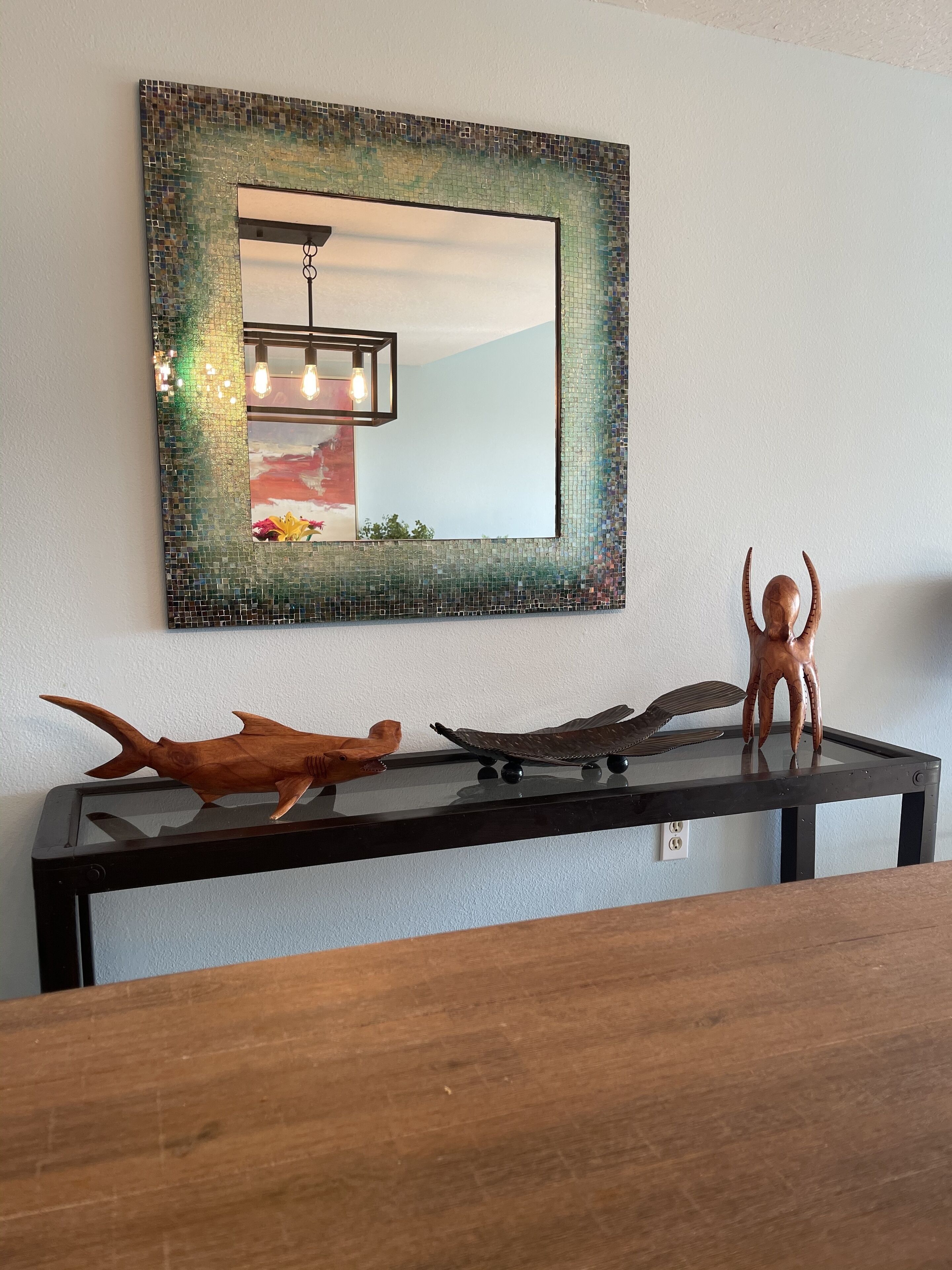 A mirror with a mosaic frame, a wooden table with decorative items, and a hanging light fixture.