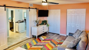 A living room with a sofa, a colorful rug, a ceiling fan, and a TV mounted on the wall. - 3 bedroom condo in cocoa beach (Cocoa Beach)