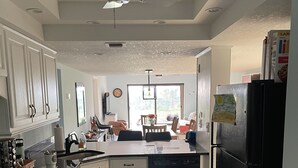 A kitchen with white cabinets, a black refrigerator, a stove, and a ceiling fan. - 3 bedroom condo in cocoa beach (Cocoa Beach)