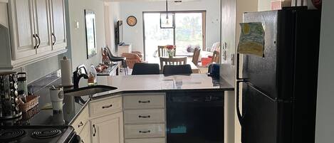 Una cocina con armarios blancos, un refrigerador negro, una estufa y un ventilador de techo.