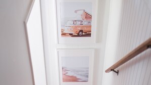 Un escalier avec une rampe en bois, des murs blancs et deux tableaux encadrés représentant un camion et une scène de plage.