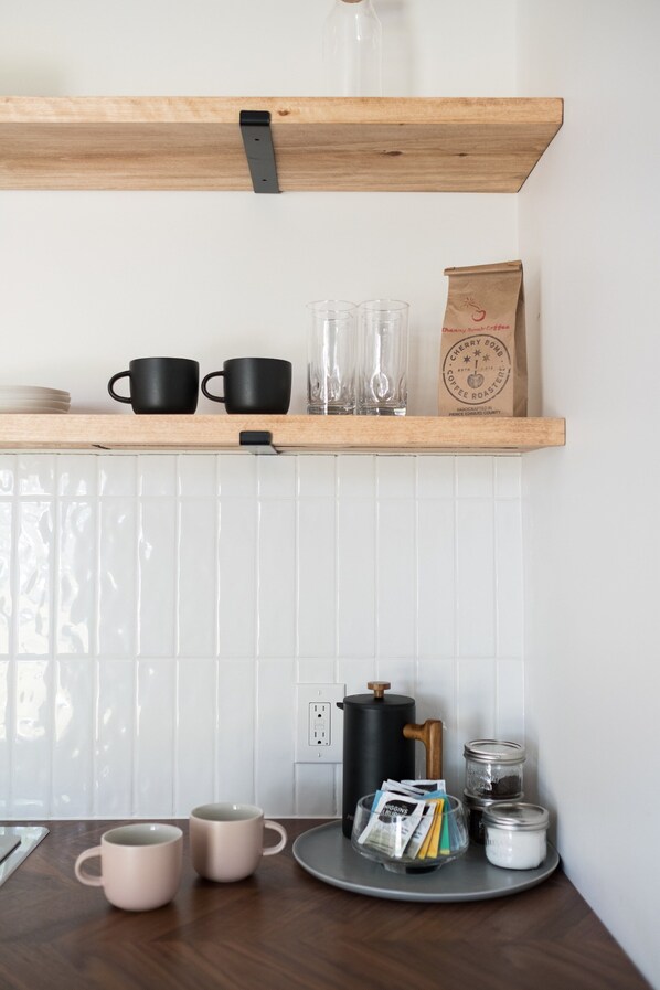 A kitchen with wooden shelves, a coffee maker, and a tray with mugs and coffee beans.