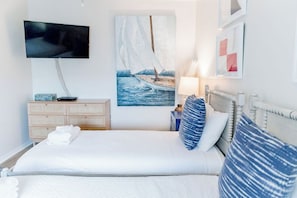 A hotel room with a bed, a television, a painting of a sailboat, and a nightstand with a lamp.