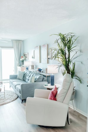 A living room with a sofa, armchair, and a large potted plant.