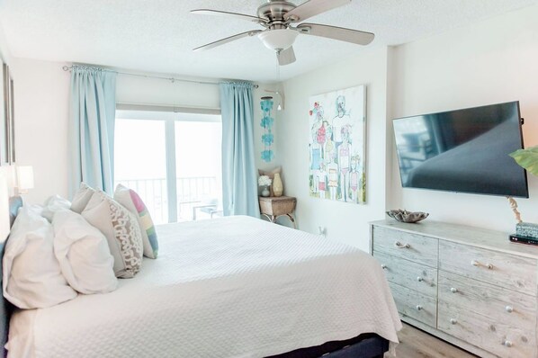 A bedroom with a bed, a ceiling fan, a TV, and a window with curtains.