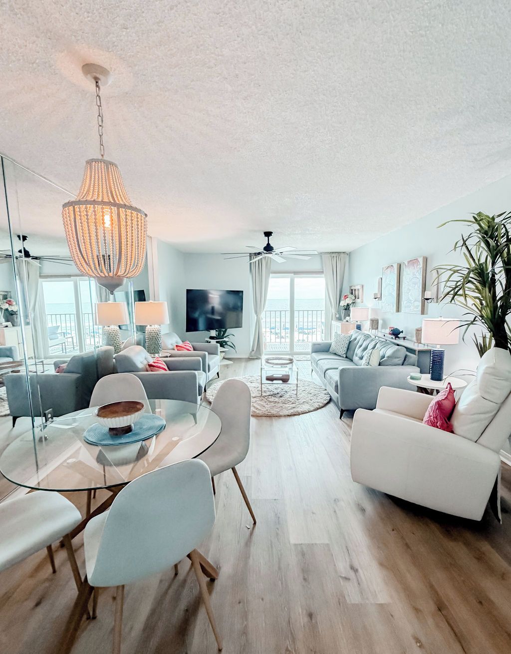 A modern living room with a glass dining table, two sofas, a white armchair, and a large chandelier.