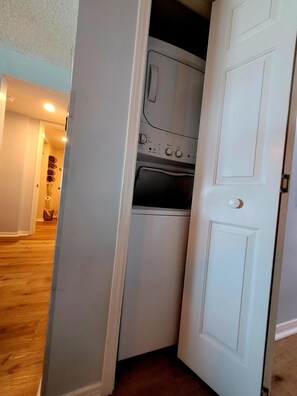 A compact laundry room with a built-in washer and dryer, a white door, and a wooden floor.
