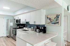 A modern kitchen with white cabinets, a central island, a microwave, a stove, and a coffee maker.