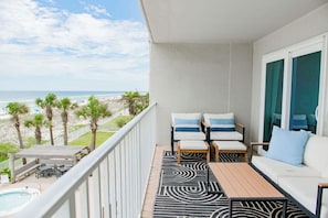 A balcony with a pool, outdoor seating, and a view of the beach.