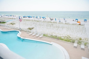 A swimming pool adjacent to a beach area with umbrellas and lounge chairs.