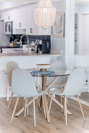 A modern dining area with a glass table, light grey chairs, and a wooden floor. - Gulf Front 2/2 | 20 Ft Balcony | On the Beach (Gulf Shores)
