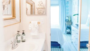 Ett hotellbadrum med ett handfat, två tvålautomater, en handduk, en spegel och en dekorativ vas.