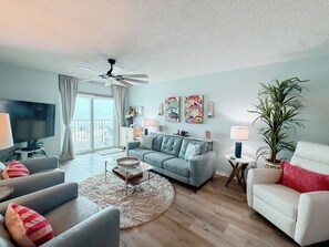A living room with a sofa, armchairs, a coffee table, a TV, a ceiling fan, artwork on the wall, and a plant. - Gulf Front 2/2 | 20 Ft Balcony | On the Beach (Gulf Shores)