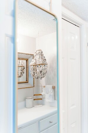 A bathroom with a white vanity, a mirror with a gold frame, a hanging light fixture, and a towel rack.