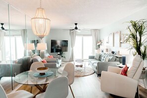 A modern living room with a glass coffee table, sofas, a TV, and a ceiling fan.