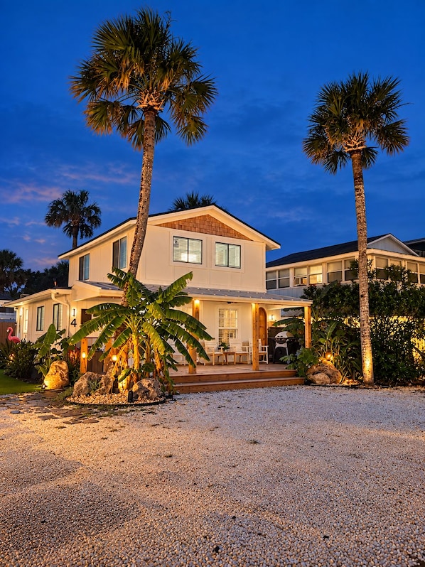 A two-story house with a patio area, palm trees, and a gravel driveway.