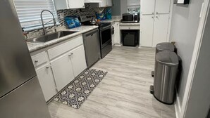 A modern kitchen with white cabinets, stainless steel appliances, and a patterned rug. - Beautifully remodeled home steps away from the Beach! (Jacksonville Beach)